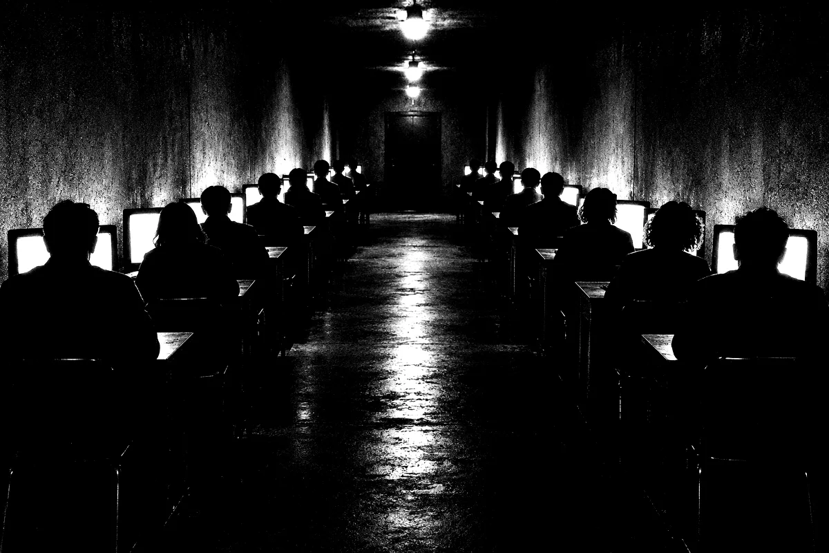 A dark hall of people at identical screens