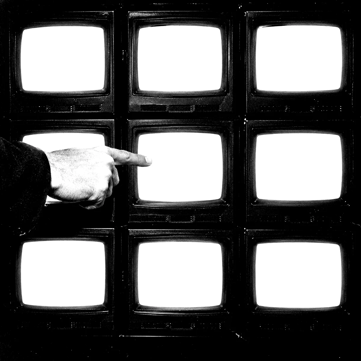 A hand pointing at one screen in a wall of nine